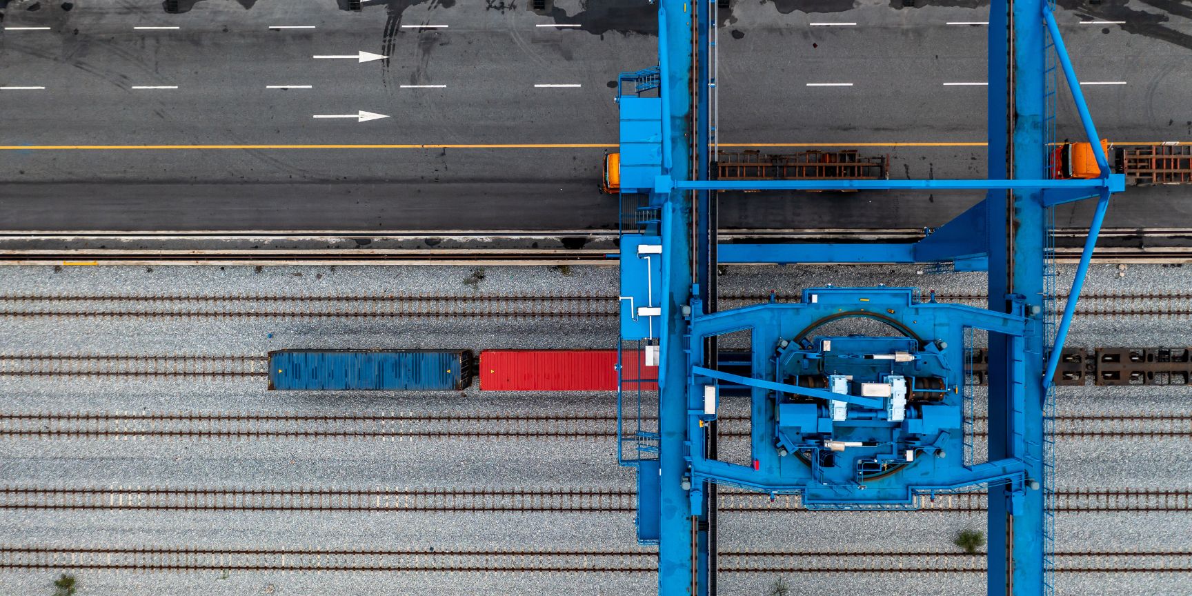 Aufnahme eines DUSS-Terminals von oben. Ein Portalkran überspannt zahlreiche Gleise, auf denen Güterzüge beladen werden. Auf den Fahrspuren daneben warten LKWs. Die Szene zeigt die enorme Skalierung des Kombinierten Verkehrs